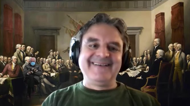 A smiling man with headphones has a background of the historic image from the signing of the Declaration of Independence, and subtly inserted on the left side is the image of Bernie Sanders sitting with arms folded